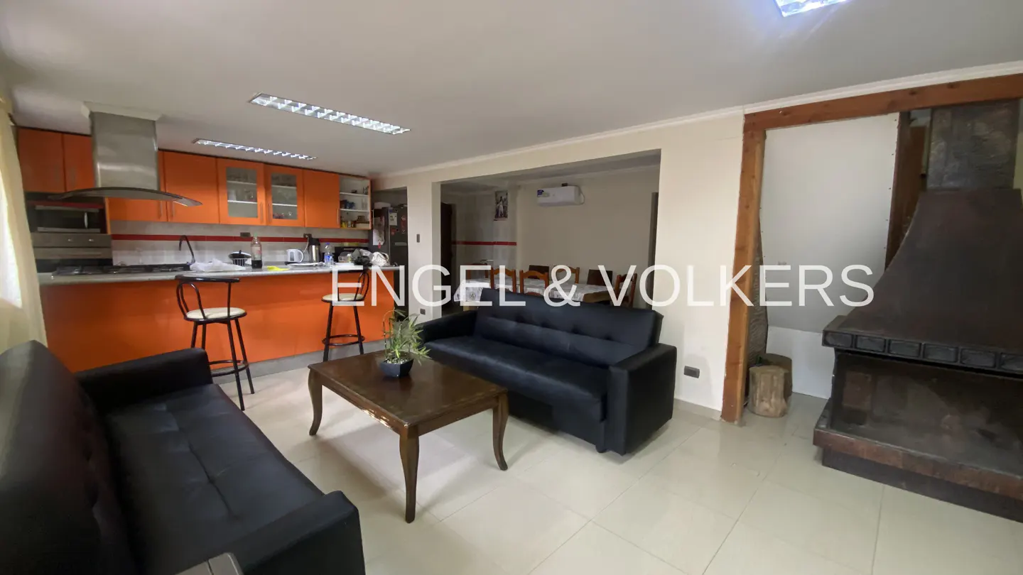A living room with black sofas, a wooden coffee table, and an orange kitchen in the background.