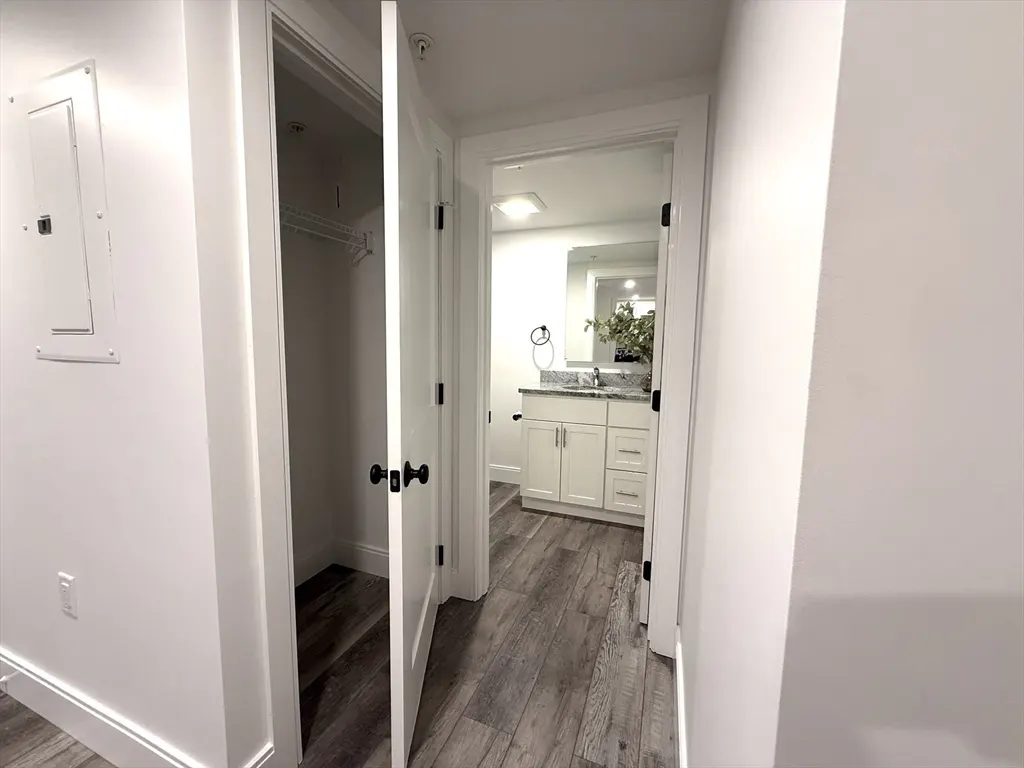 Hallway with open white doors to a closet and bathroom with white vanity and gray wood-look flooring.