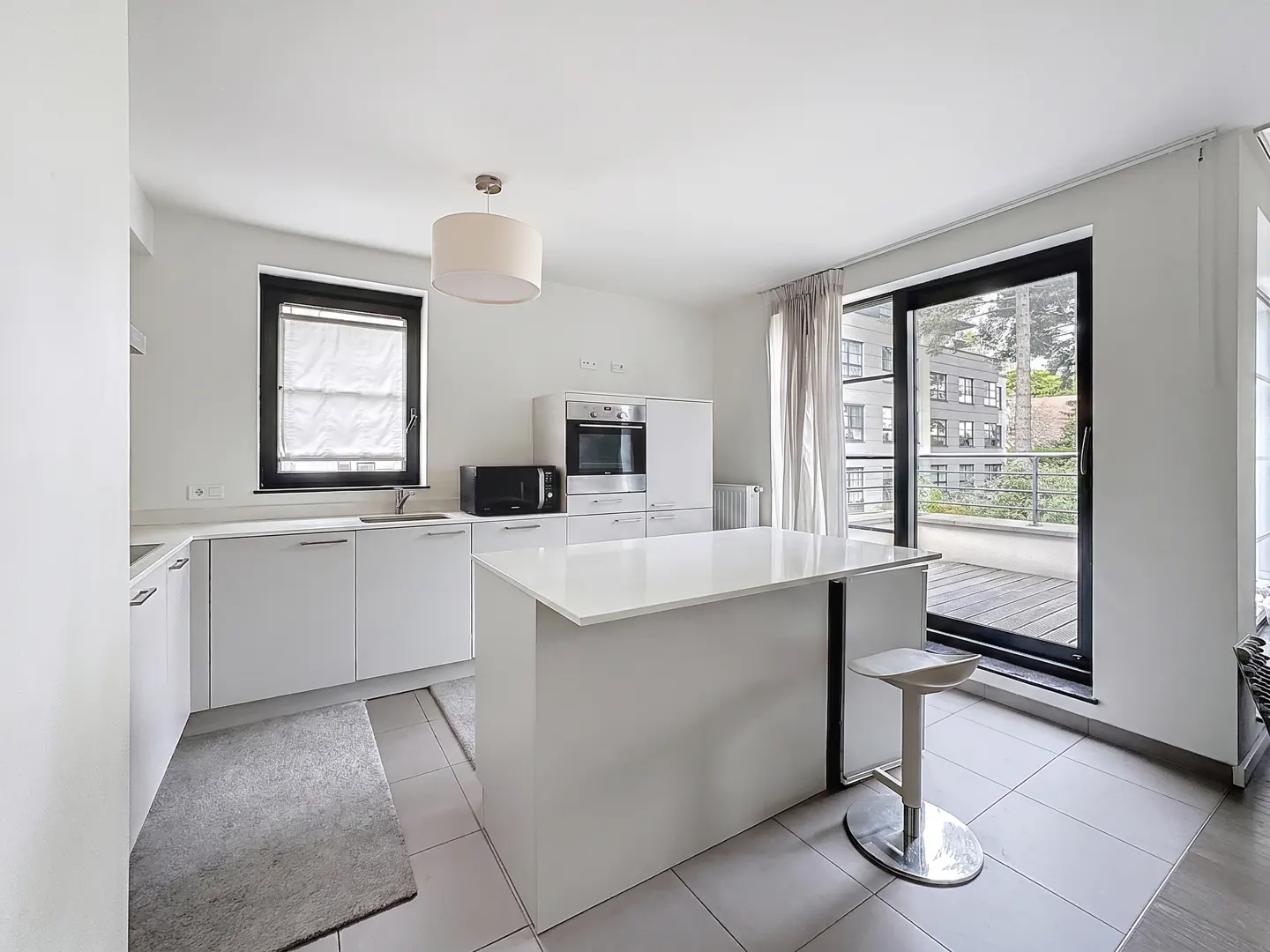 Bright, modern kitchen with white cabinets, island, and stainless steel appliances. A large window and sliding glass door lead to a balcony.