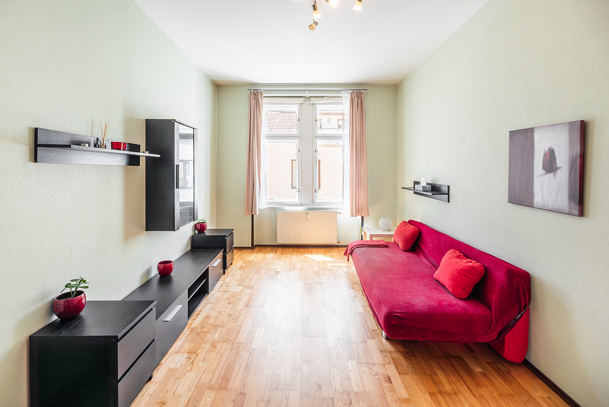 A bright living room with light green walls, wood floors, a red sofa, and black modular storage units under a window.