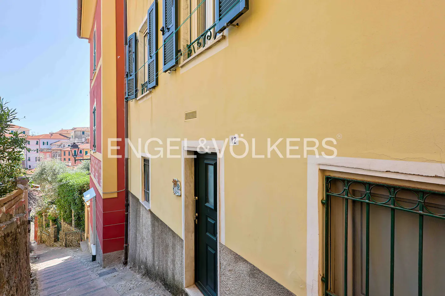 Exterior view of a yellow building with green shutters and door, and the Engel & Völkers logo.