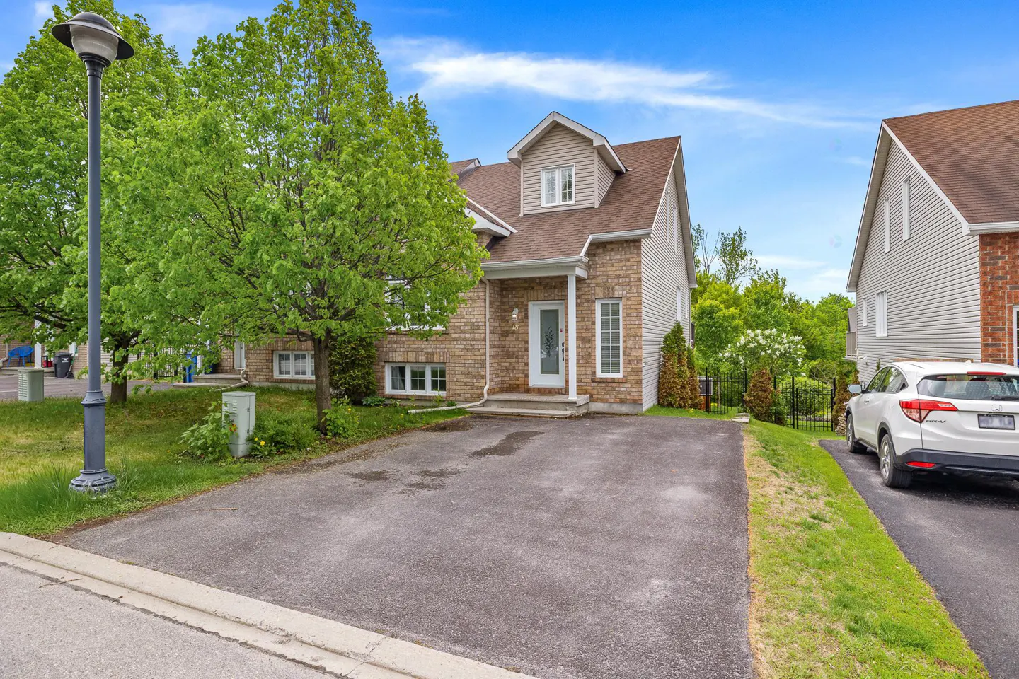 A two-story brick and siding house with a paved driveway, a white front door, and a white SUV parked on the side.
