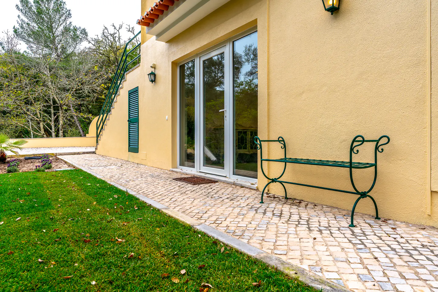 Exterior of a yellow house with a green bench, white door, and stone walkway.