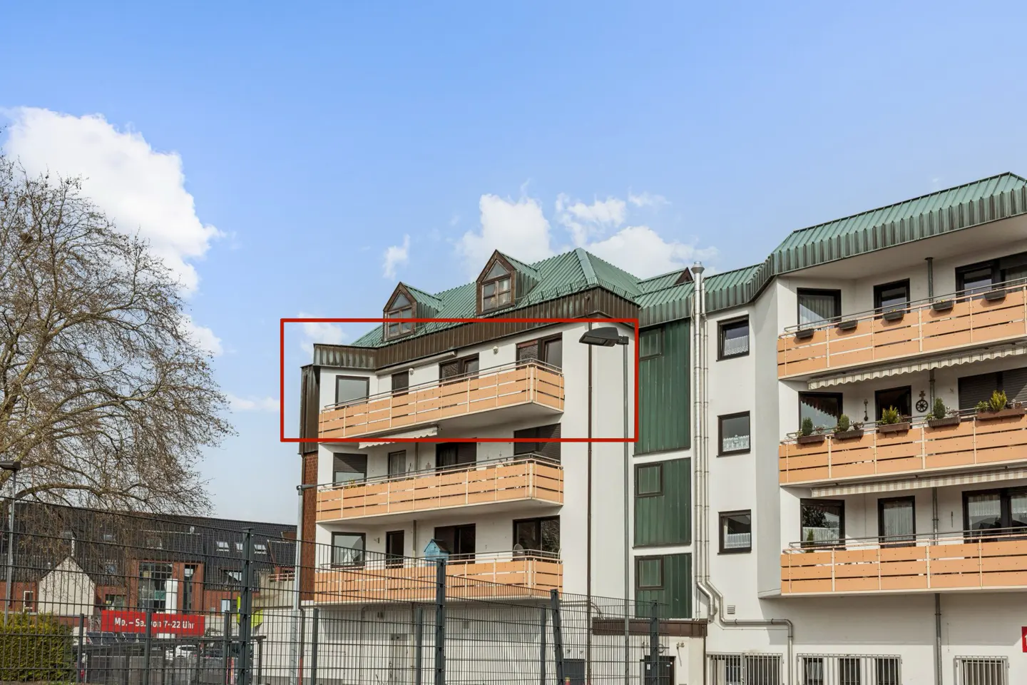 Exterior of a white apartment building with balconies and a green roof under a blue sky.