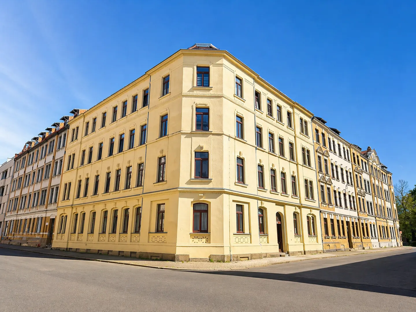 A low-angle shot of a yellow apartment building with dark windows under a clear blue sky.