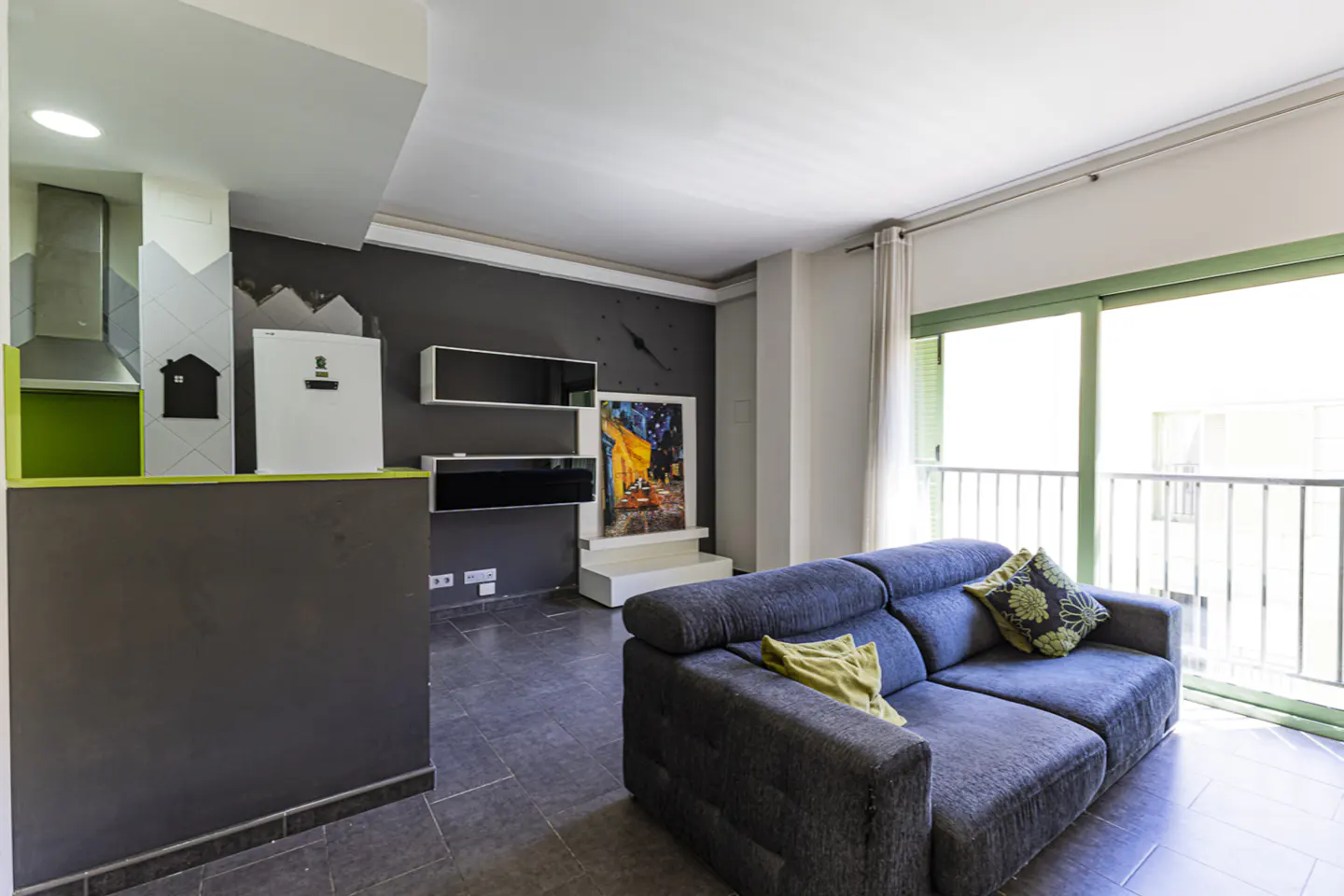 Living room with gray walls, blue sofa, and sliding glass doors to a balcony. Abstract art and floating shelves on the wall.
