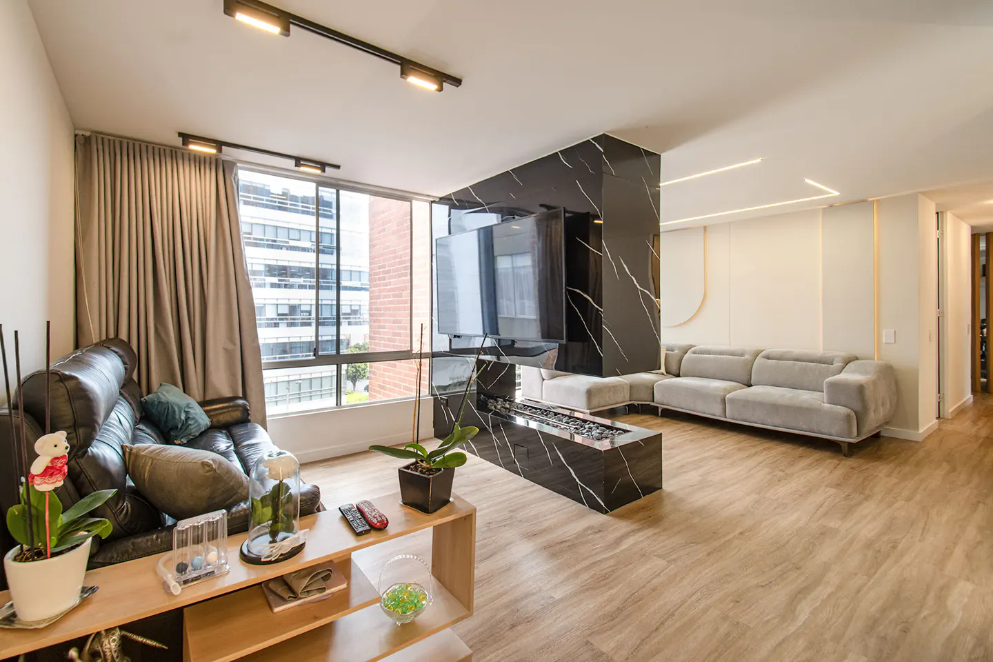 Living room with a black leather sofa, a gray sofa, a black marble fireplace, and a light wood floor.