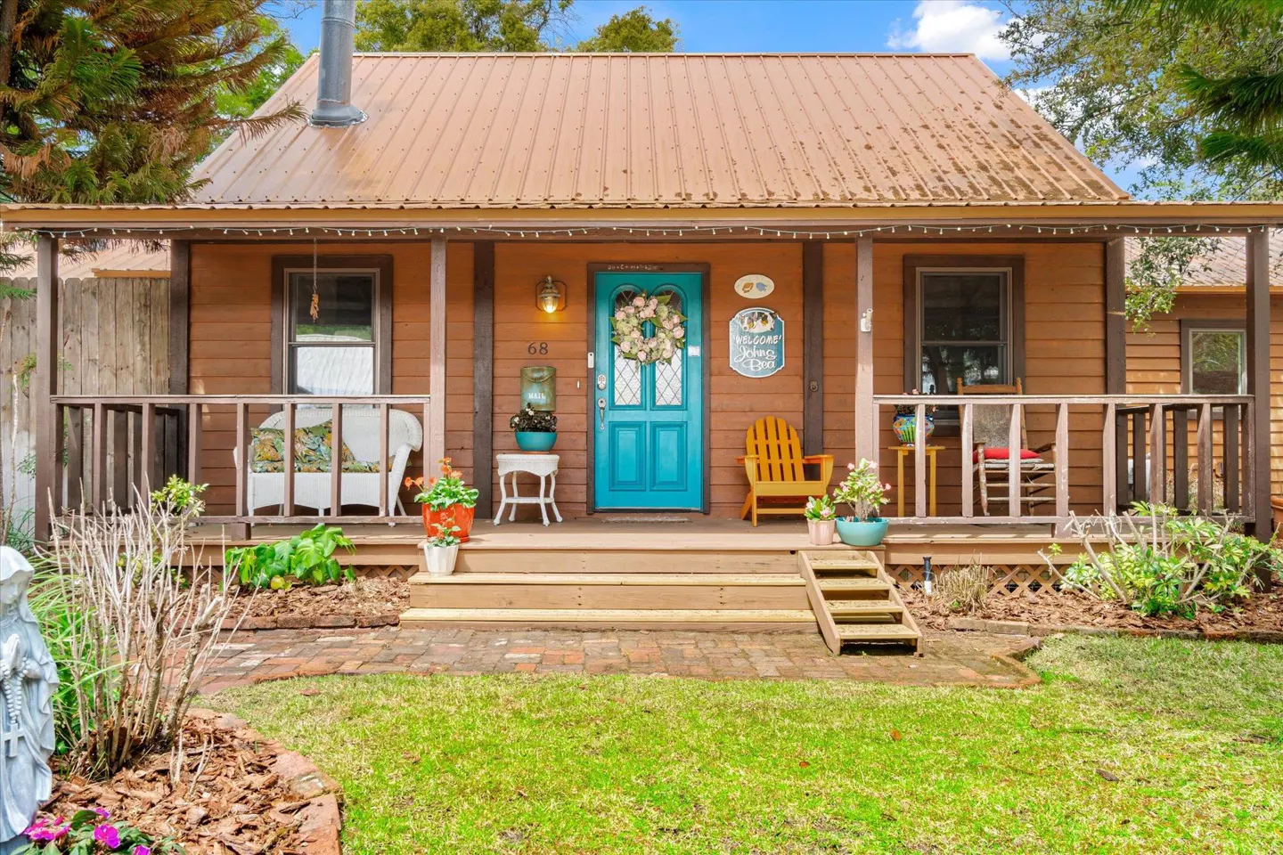 Charming brown house with a teal door and metal roof. A porch with chairs and plants adds to the cozy curb appeal.