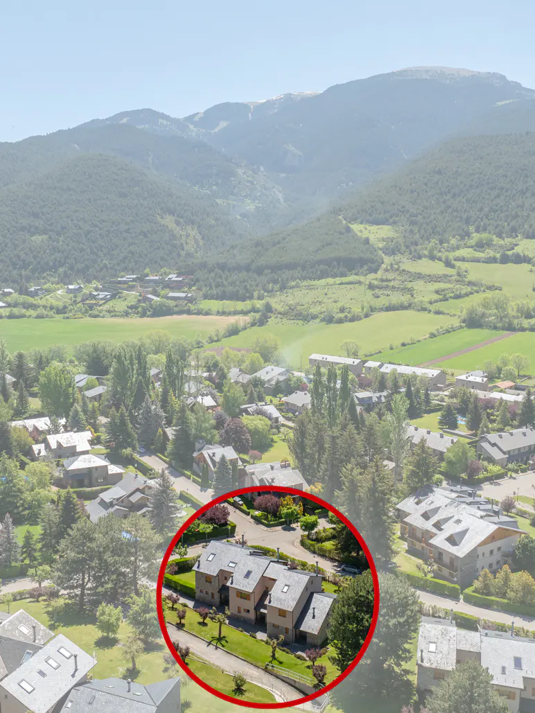 Aerial view of a beige house with a gray roof, green lawn, and trees, circled in red, with mountains in the background.