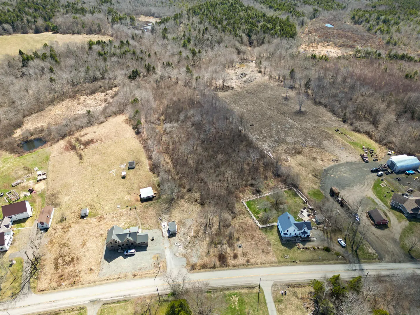 Aerial view of rural land with houses, fields, and woods. A road runs through the bottom of the frame.