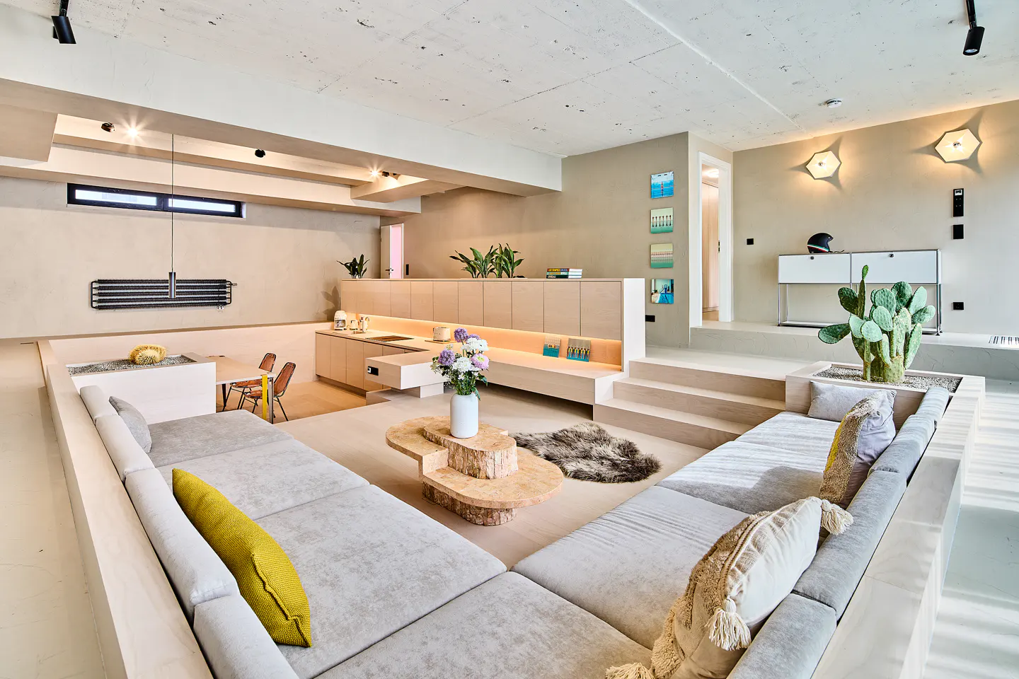 Modern sunken living room with light gray sectional sofas, a tiered wooden coffee table, and a built-in kitchen area.