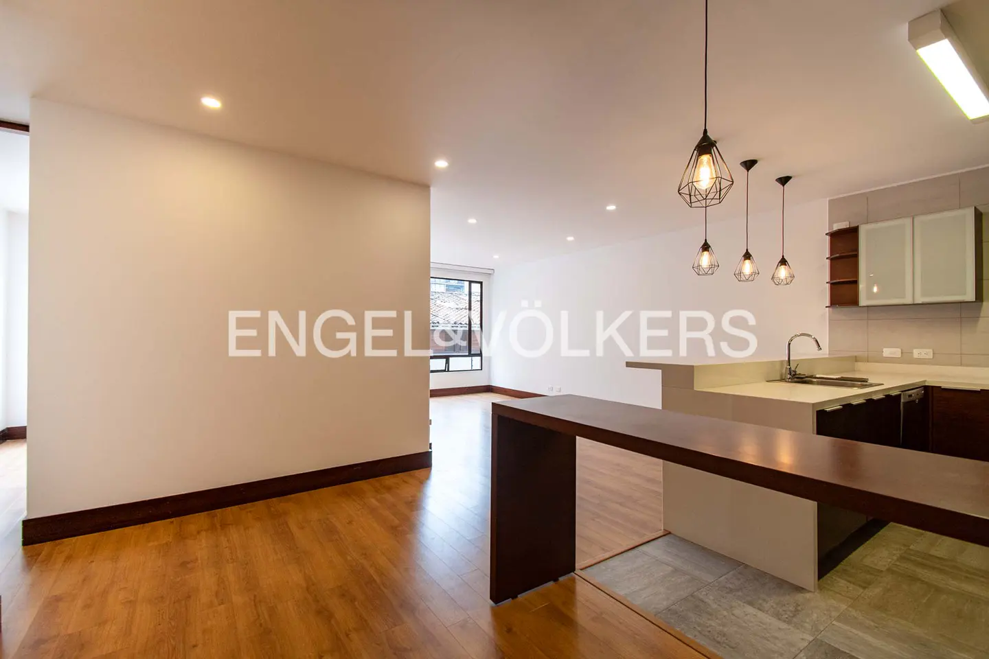 A bright, modern apartment interior with hardwood floors, a kitchen with pendant lights, and the Engel & Völkers logo.