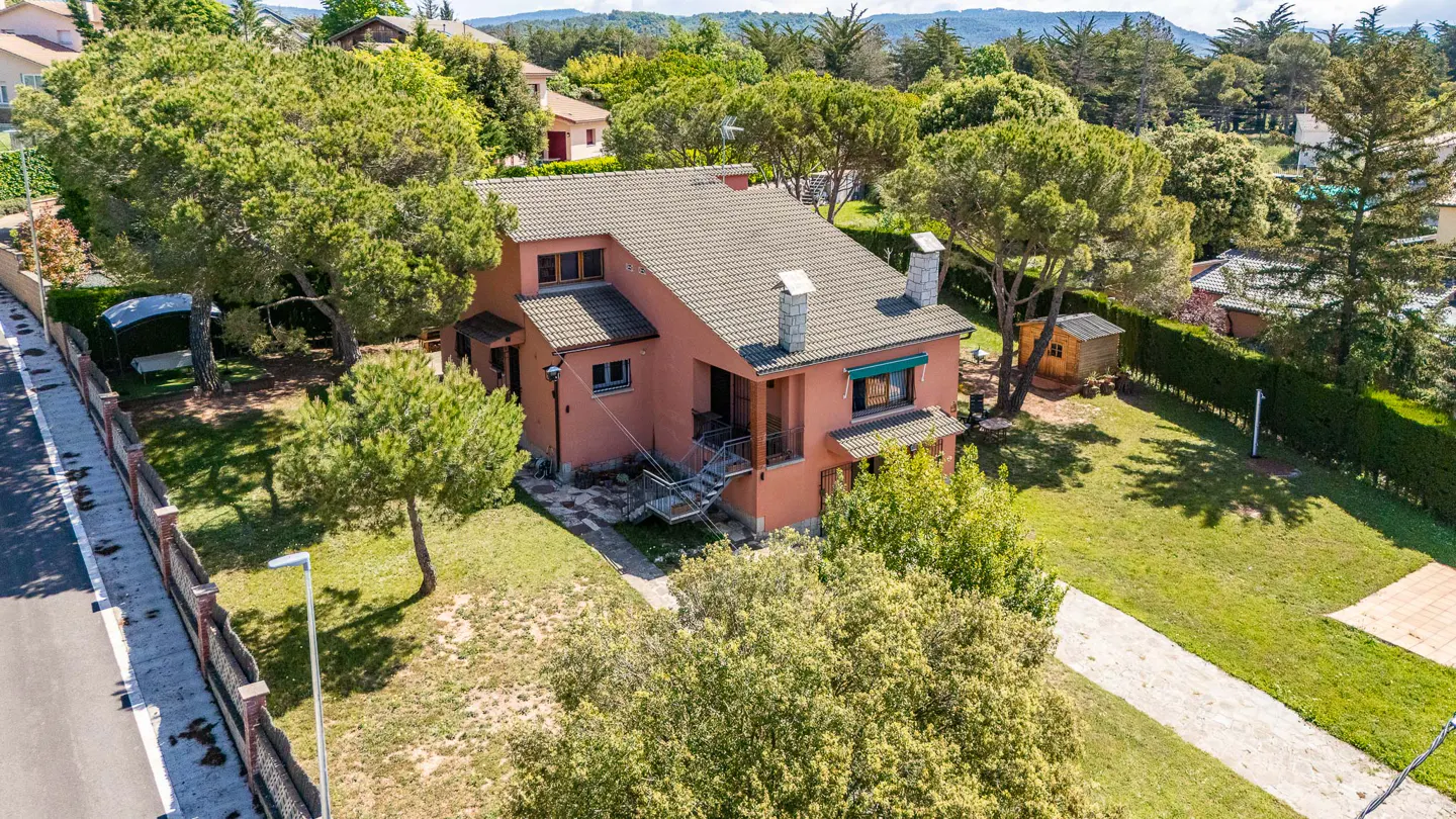 Aerial view of a two-story salmon-colored house with a gray roof, surrounded by green trees and a well-maintained lawn.