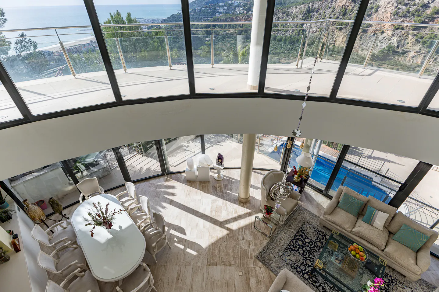 Bird's eye view of a modern home interior with a dining table, sofa, and large windows overlooking the ocean.