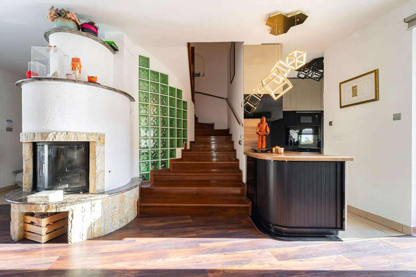 Interior view of a home featuring a fireplace, wooden stairs with green glass blocks, and a kitchen counter.