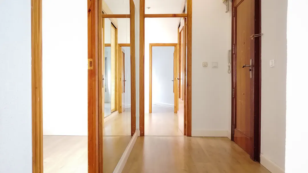 Hallway view with light wood floors, white walls, and multiple open wood-framed doorways leading to other rooms. A brown front door is on the right.