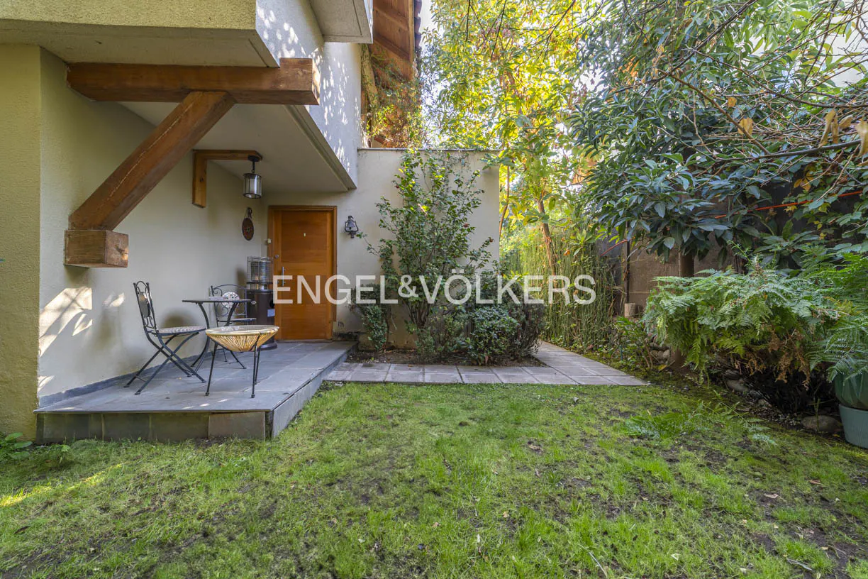 Exterior view of a house with a small patio, table, chairs, and green lawn. The Engel & Völkers logo is visible.
