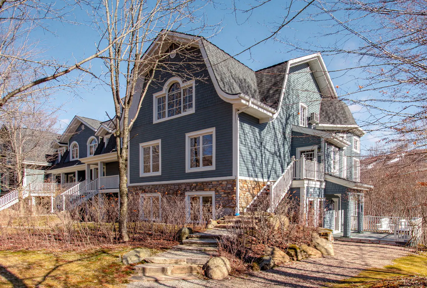 Exterior of a blue, multi-story house with a stone foundation and a curved roof. White trim accents the windows and stairs.