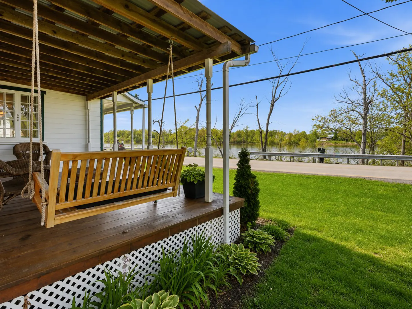 Porch view with a wooden swing hanging from the ceiling, overlooking a green lawn and a lake in the background.