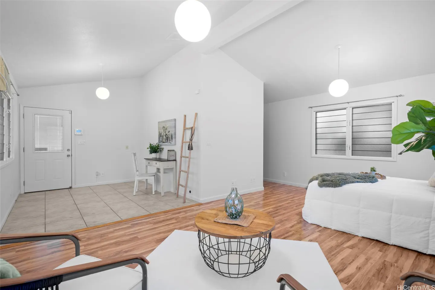 Bright, airy living space with white walls, wood floors, and modern furniture. Desk, ladder, and bed visible.