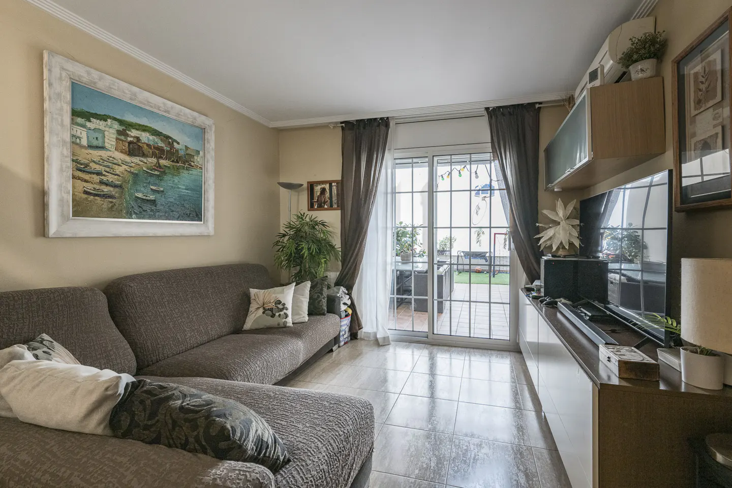 Living room with a brown sectional sofa, a painting of a seaside village, and sliding glass doors to a patio.