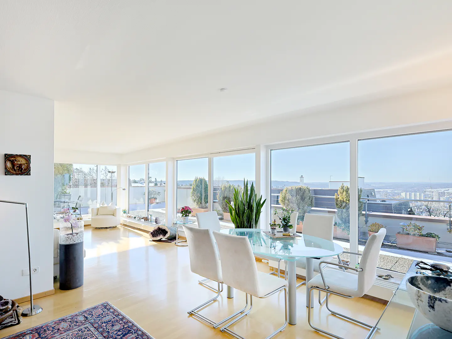 Bright dining area with a glass table, white chairs, and large windows overlooking a sunny outdoor terrace.