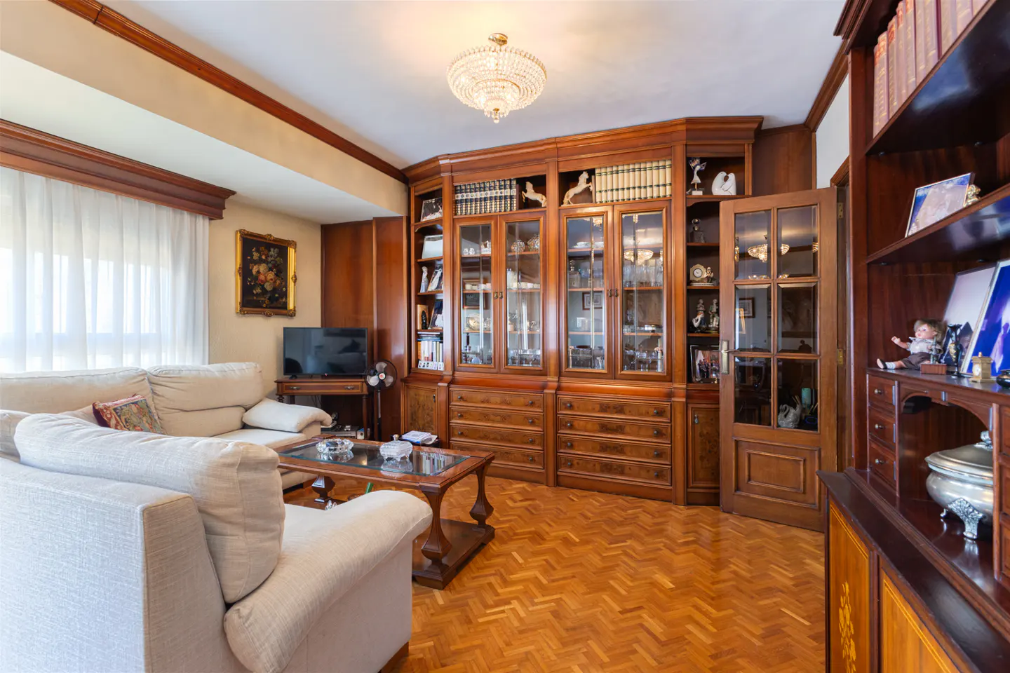 Living room with a large wooden bookcase filled with books and decorative objects, a white sofa, and a herringbone wood floor.