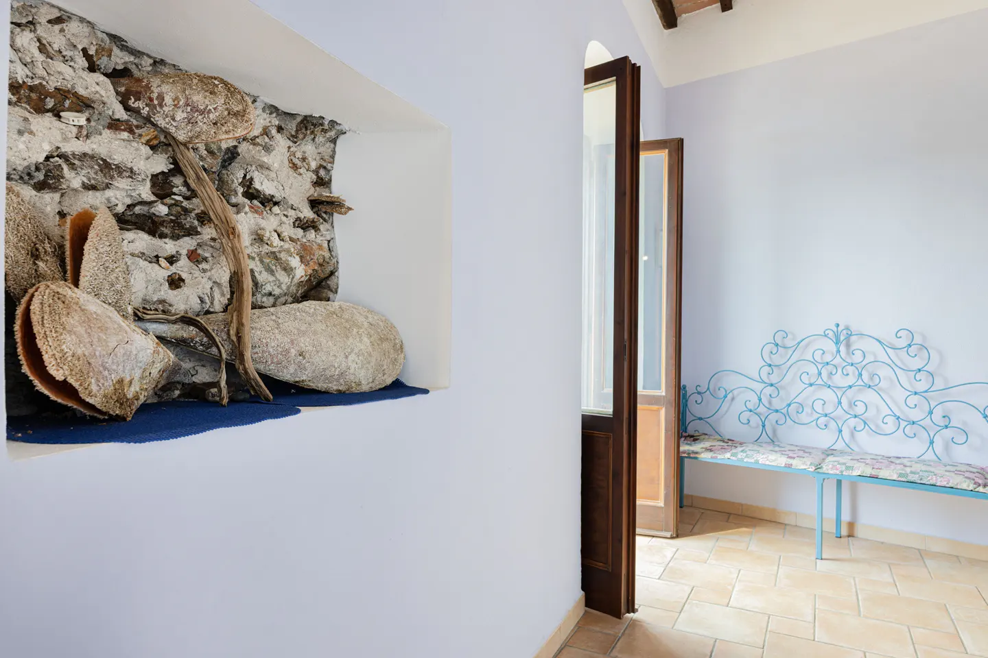 Interior view of a room with a stone niche, shells, and a blue wrought-iron bench.