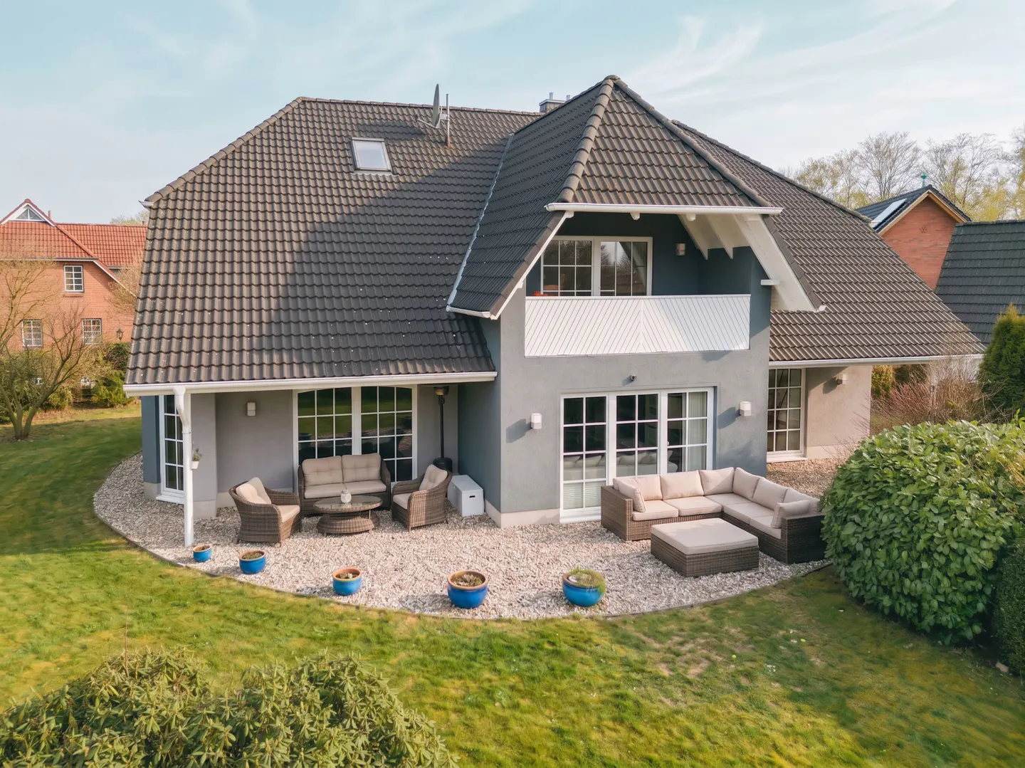Aerial view of a gray two-story house with a dark gray tiled roof and a patio with outdoor furniture.