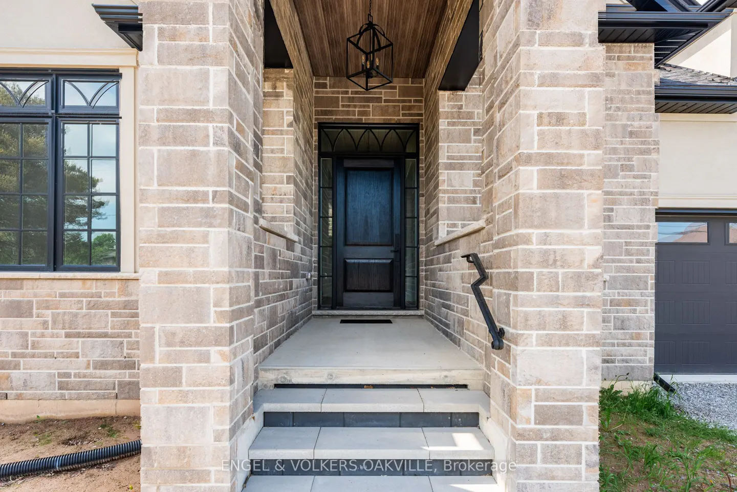 Stone facade of a home with a black front door, black window frames, and a black handrail.