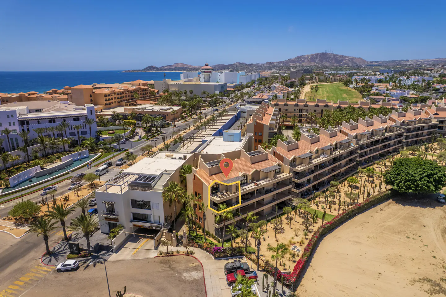 Aerial view of a condo building with a red pin and yellow outline, near the ocean and mountains.