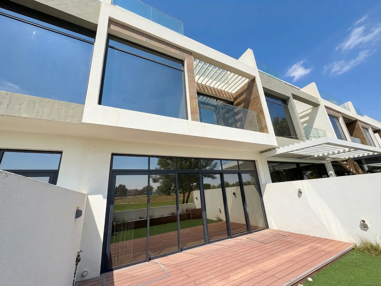 Modern townhouse exterior with large windows, a wooden deck, and a view of a green lawn under a blue sky.
