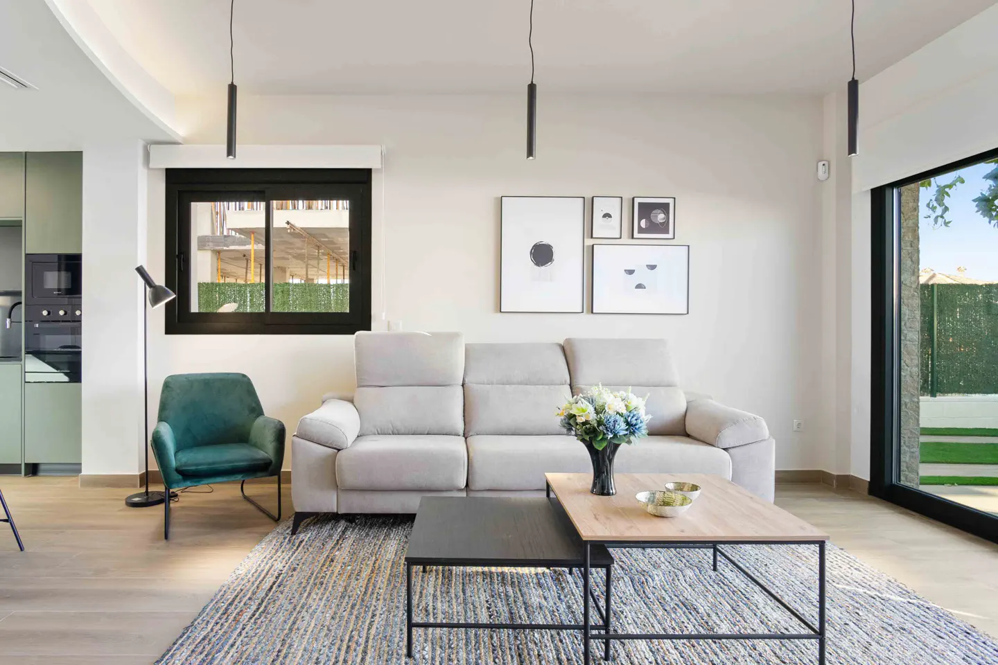 Living room with a beige sofa, green armchair, and nested coffee tables on a blue rug. Black framed art hangs above the sofa.