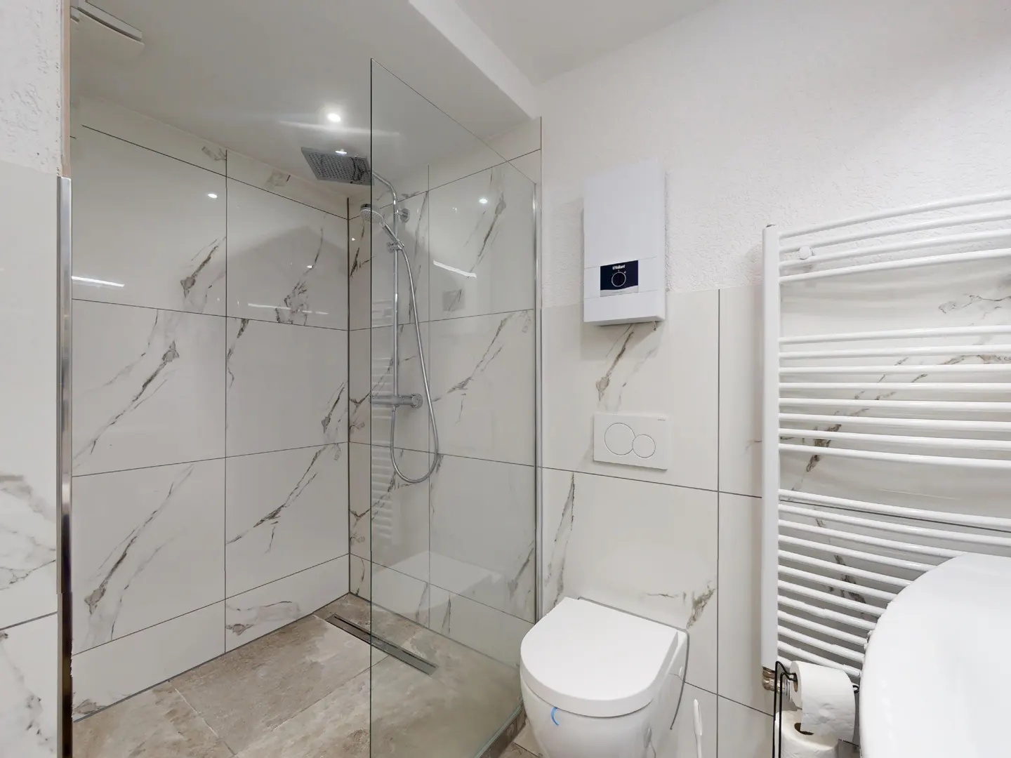 Bright bathroom with marble-patterned tile, glass shower, toilet, and white towel rack.