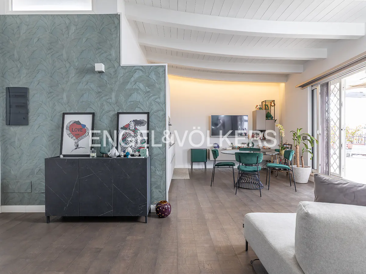 Interior view of a modern living space with a gray sofa, dining area with green chairs, and a textured green wall.