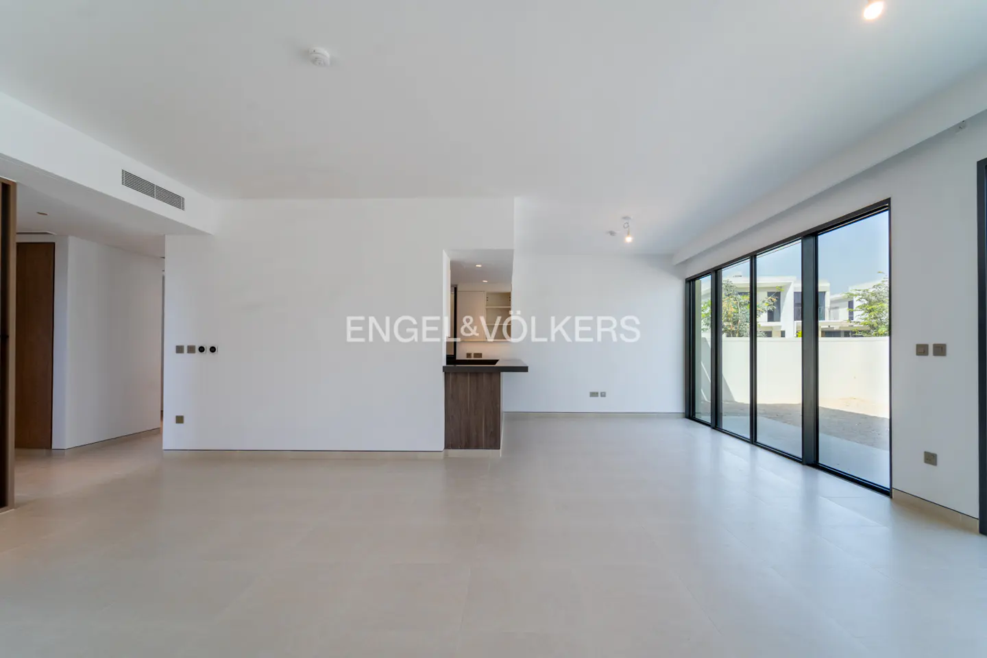 Spacious, minimalist living room with white walls, light tile floors, and large glass doors leading to an outdoor area.