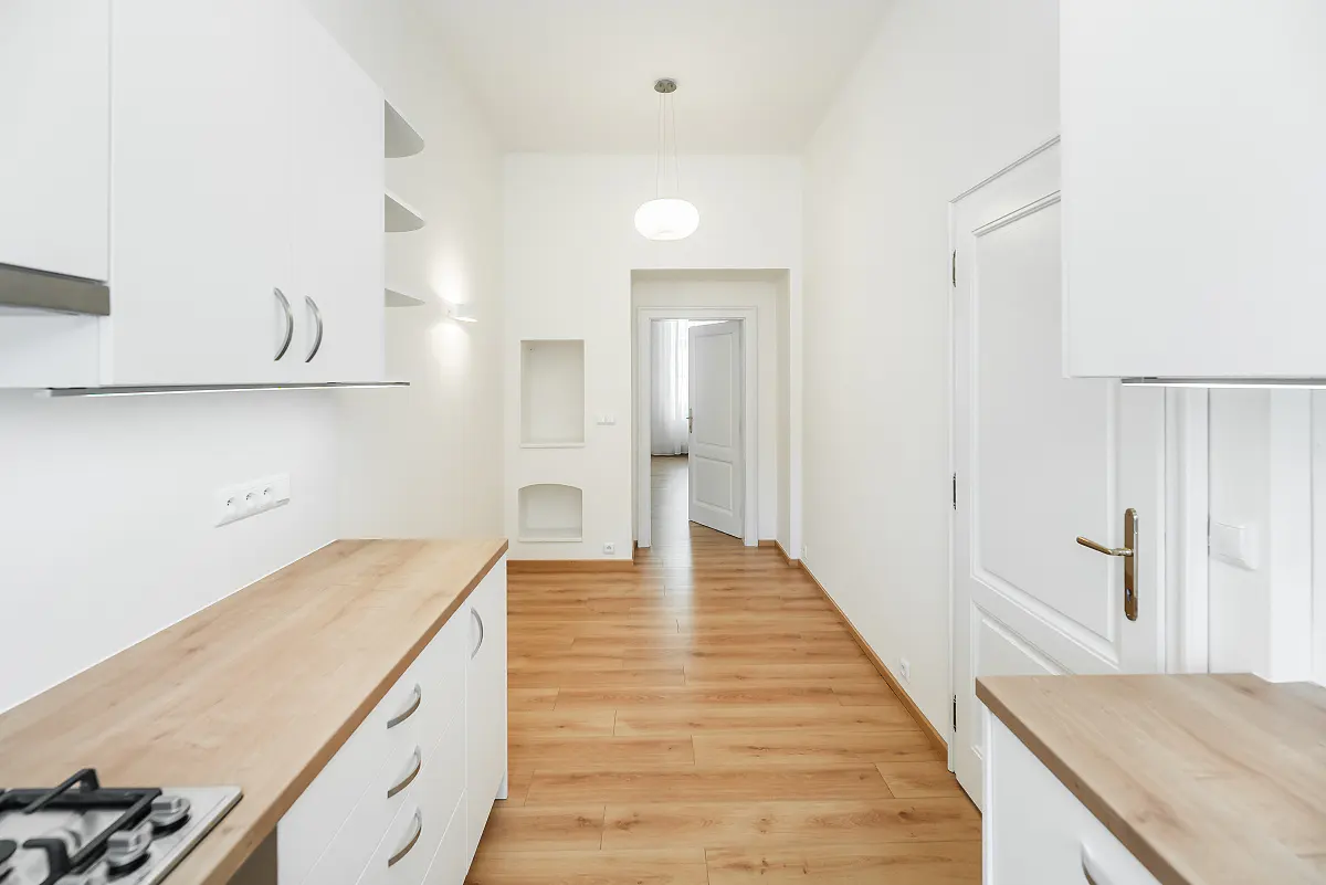 Bright, white kitchen with wood countertops and floors. An open doorway leads to another room.