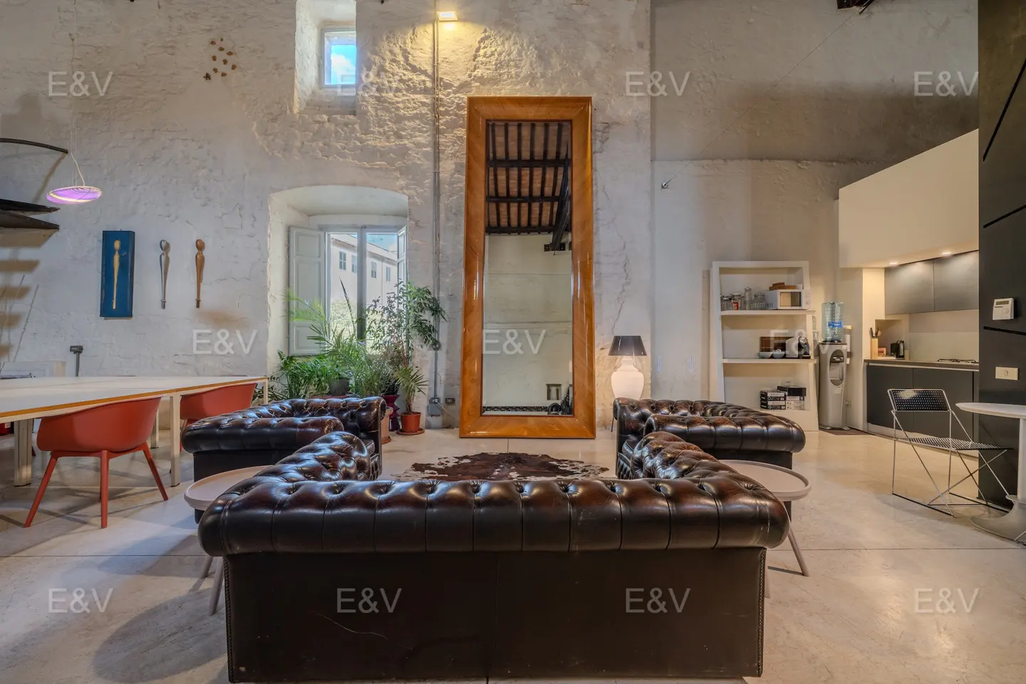Living room with brown leather sofas, a large mirror, and a dining table with orange chairs. The walls are white and textured.