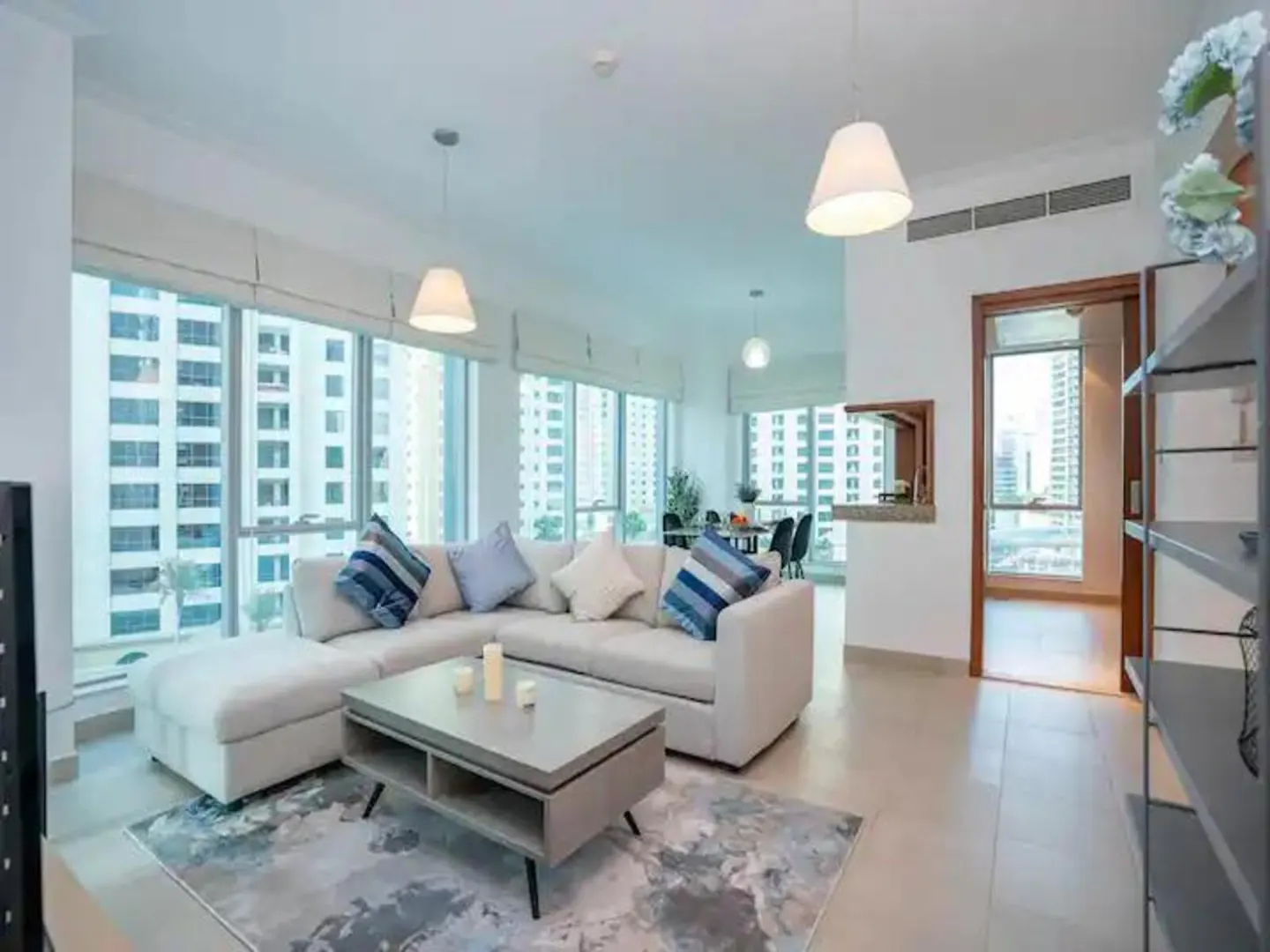 Modern living room with a white sectional sofa, grey coffee table, and large windows overlooking city buildings.