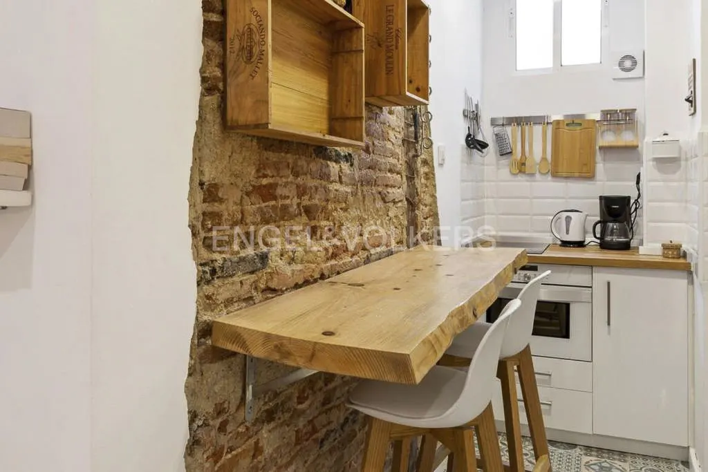 A modern kitchen with white cabinets, a wooden countertop, and a breakfast bar with two white chairs.