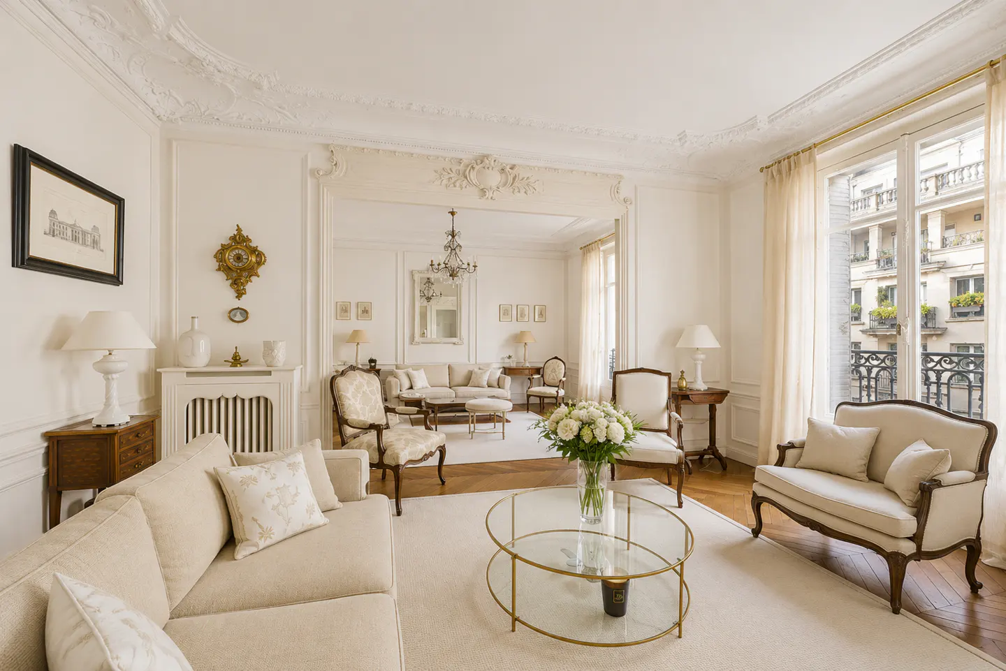 Bright, elegant living room with white walls, ornate molding, and hardwood floors. Beige sofas and chairs surround a glass coffee table. Balcony view.