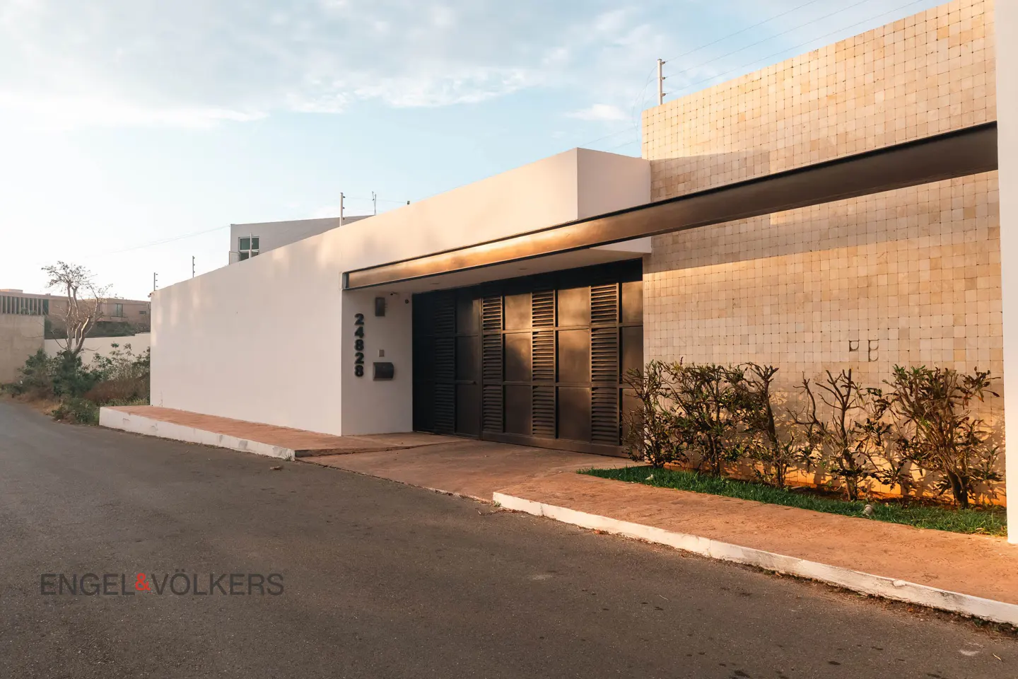Modern home exterior with a white wall, black gate, and address number 24828. A stone wall and green bushes add texture.