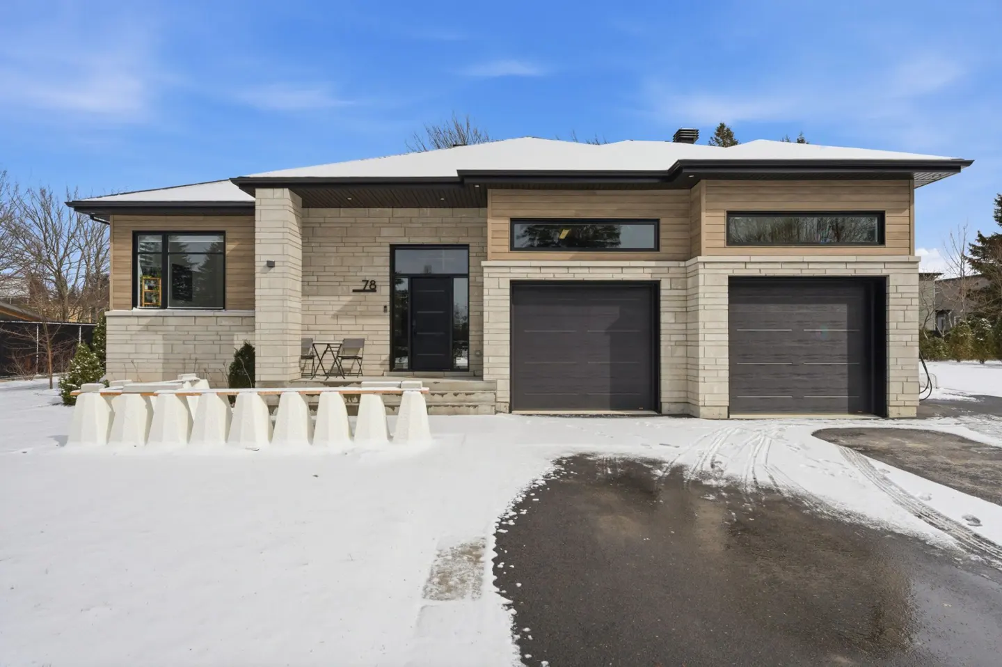 Modern two-story home with a two-car garage, stone and wood facade, black trim, and snow-covered lawn.