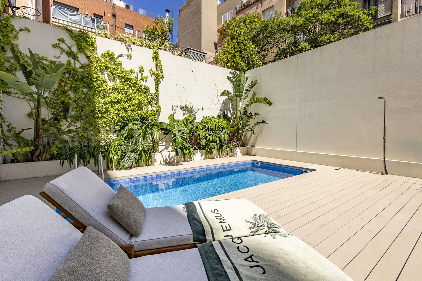 A backyard pool with two lounge chairs and a white wall covered in greenery.