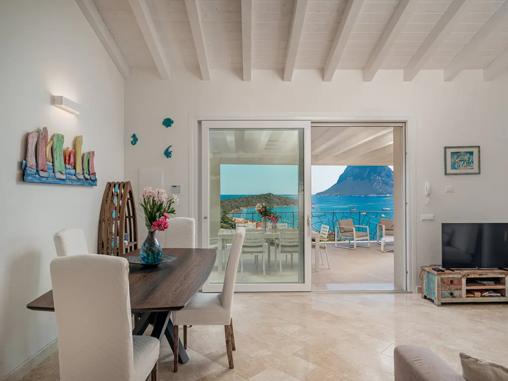 A bright dining room with a dark wood table and white chairs, leading to a patio with ocean views.