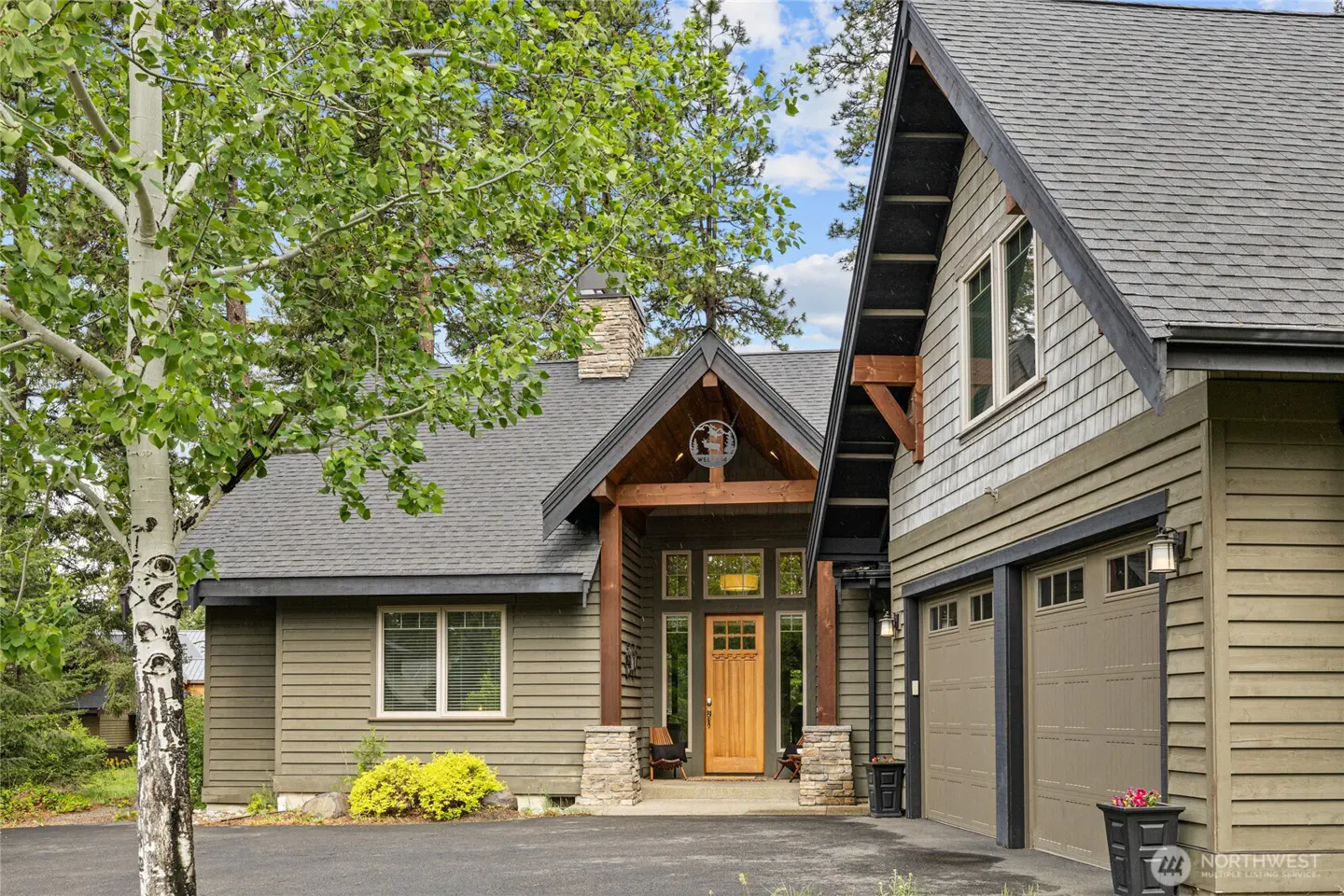 Exterior of a two-story home with a gray roof, olive green siding, and a wooden front door. A birch tree is on the left.