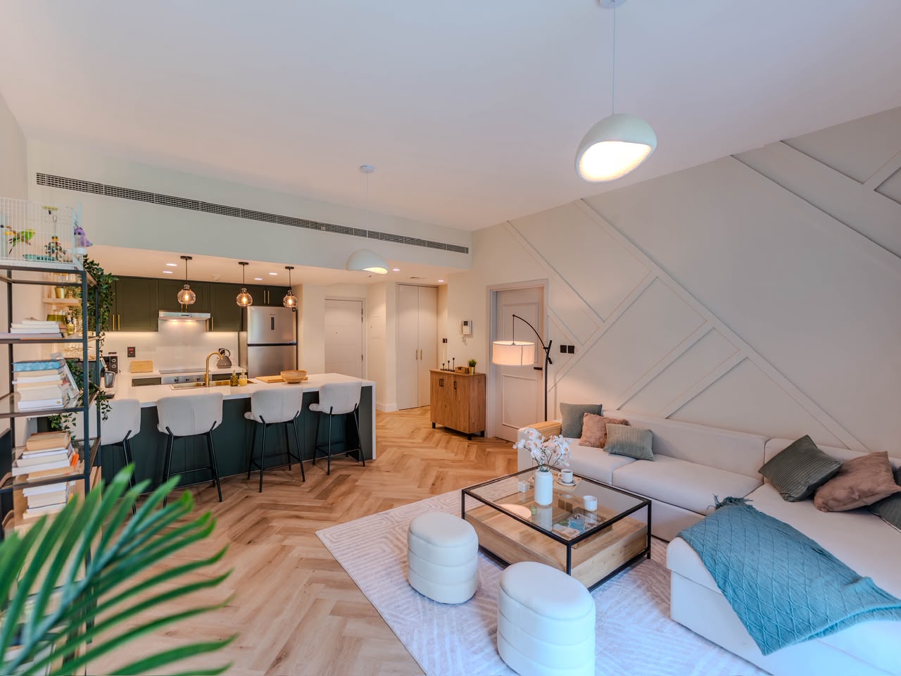 Modern open-plan living area with herringbone wood floors, white sofa, glass coffee table, and dark green kitchen island. [AI-generated text]