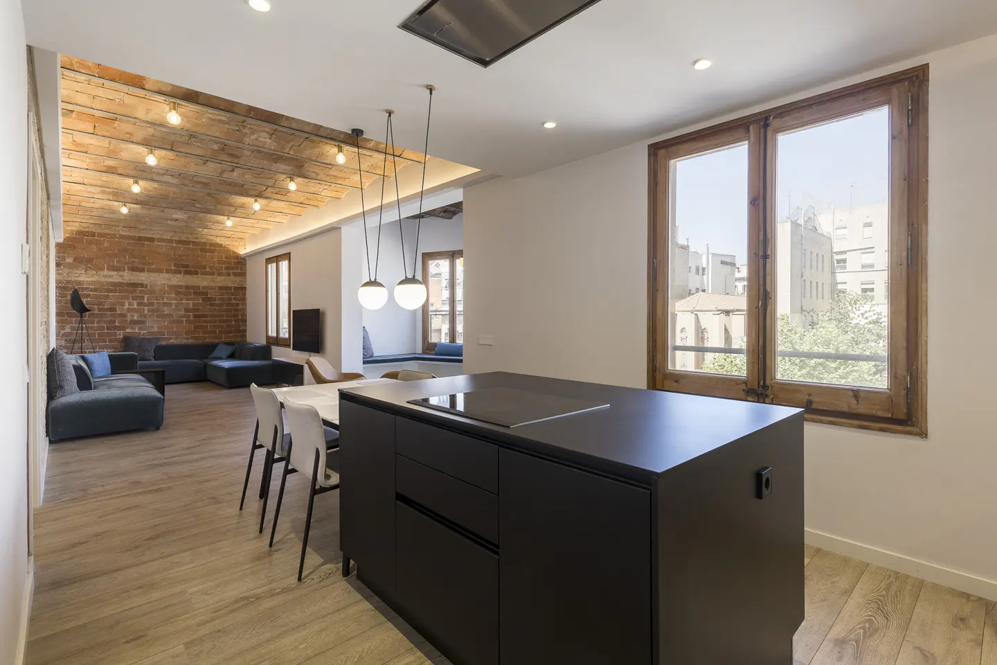 Open-concept apartment with exposed brick ceiling, black kitchen island, dining table, and blue sofa. Natural light from large windows.