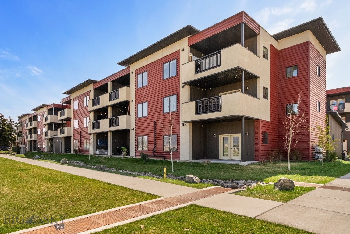 Modern three-story apartment building with red siding, beige accents, and black balconies under a blue sky.