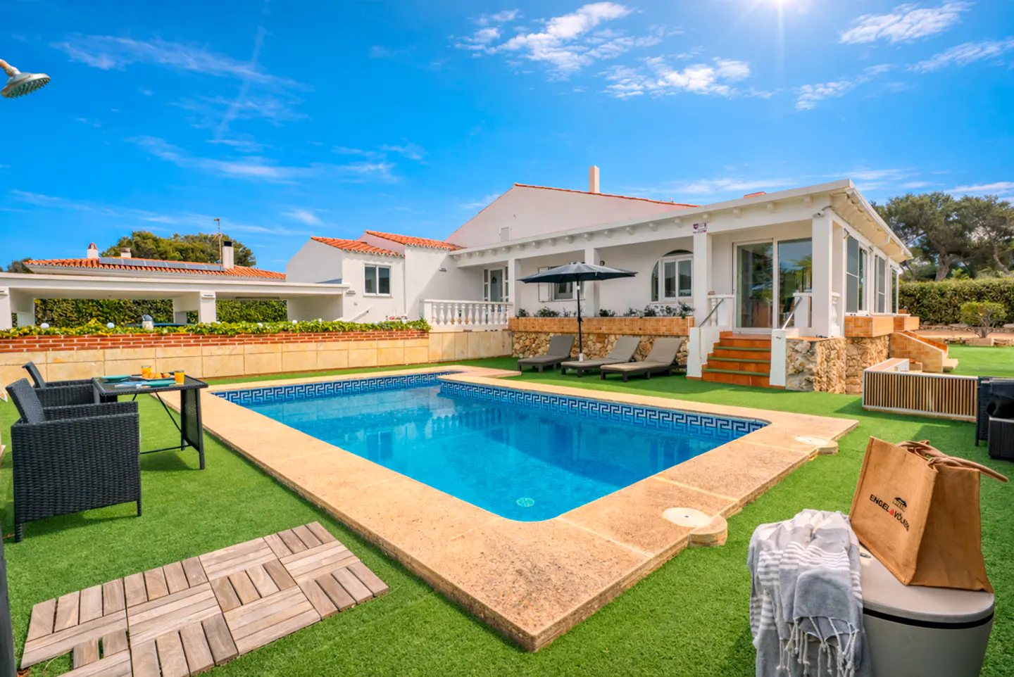 Exterior view of a white house with a pool, lounge chairs, and outdoor furniture on a sunny day.